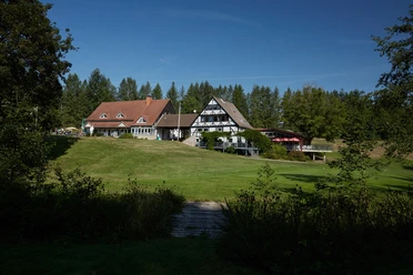 Das Clubhaus Clubhaus im Fachwerkstil mit weitläufigem Rasen, Bäumen im Hintergrund und klarem Himmel.