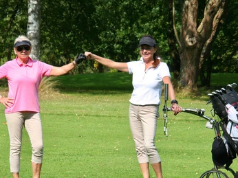 Turnierteilnehmer im Spiel Zwei Golferinnen in sportlicher Kleidung geben sich freudig die Hand auf einem Golfplatz.