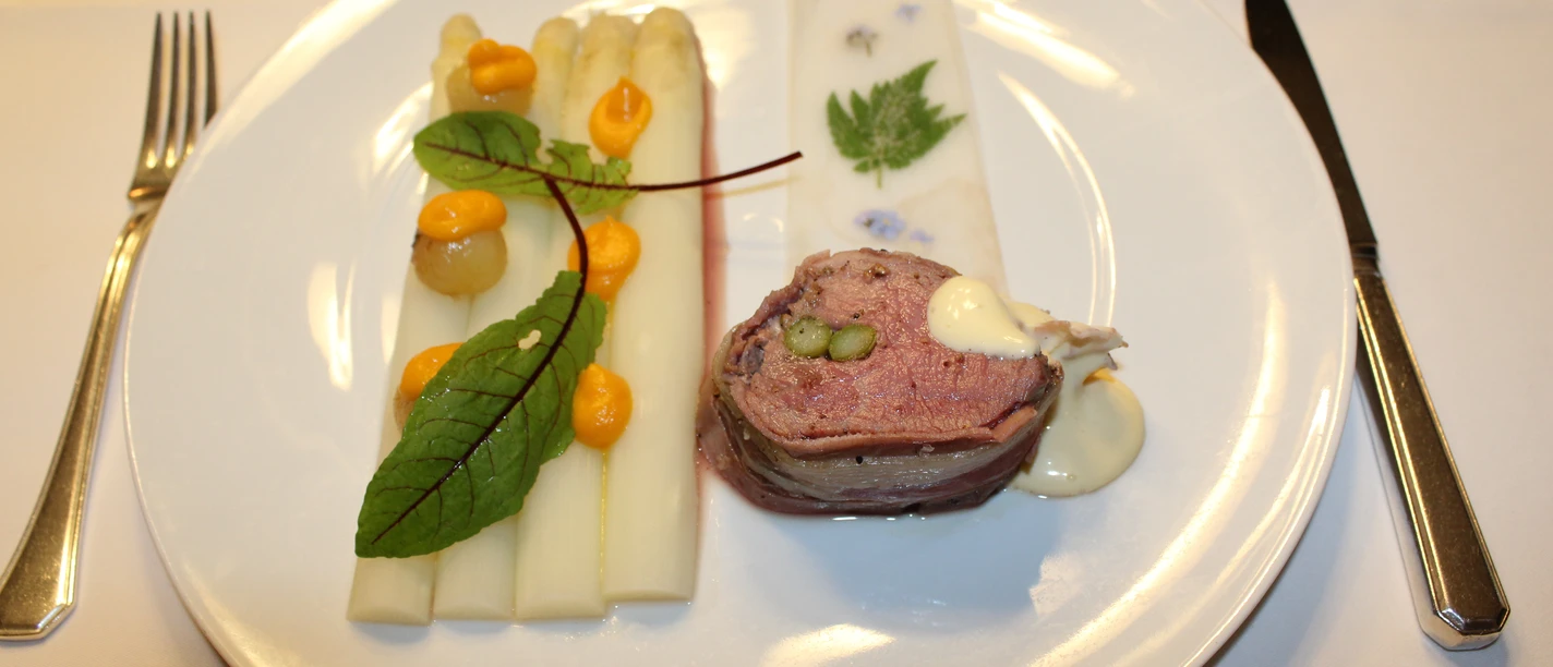 White asparagus spears with sauce and herbs, accompanied by a meat roulade on a plate.