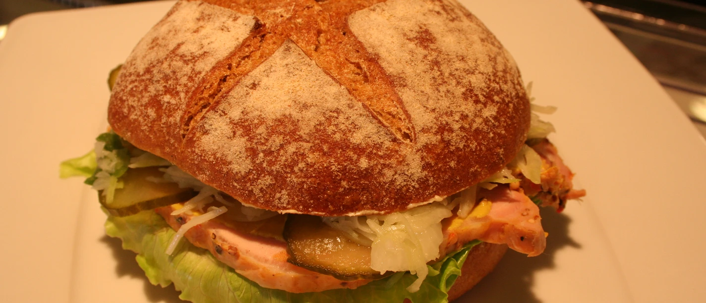 Belegtes Brötchen Ein belegtes Vollkornbrötchen mit frischem Salat, Gewürzgurke, Krautsalat und Schinken auf einem Teller.