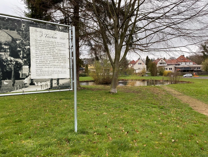 Park der 3 Teiche direkt neben dem Alten Kurpark Bad Rehburg Park mit drei Teichen, umgeben von Grünflächen und Wohnhäusern, Informationstafel im Vordergrund.