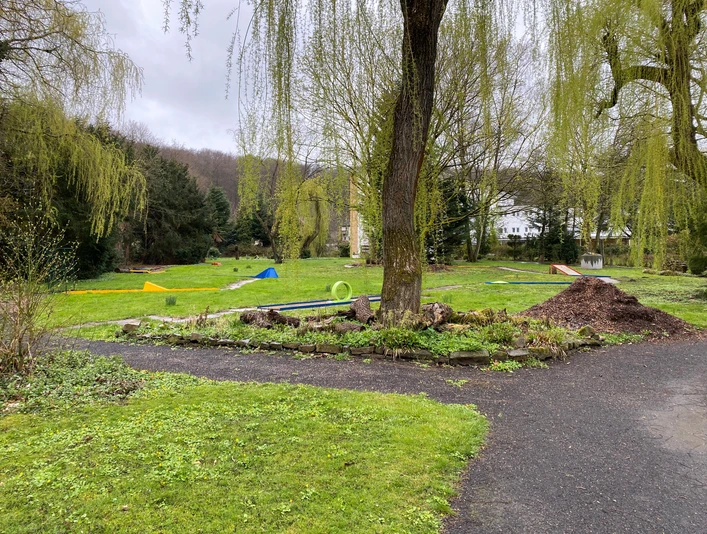 Minigolfanlage in einem grünen Park mit Bäumen und gewundenen Wegen, entspannter Freizeitort.