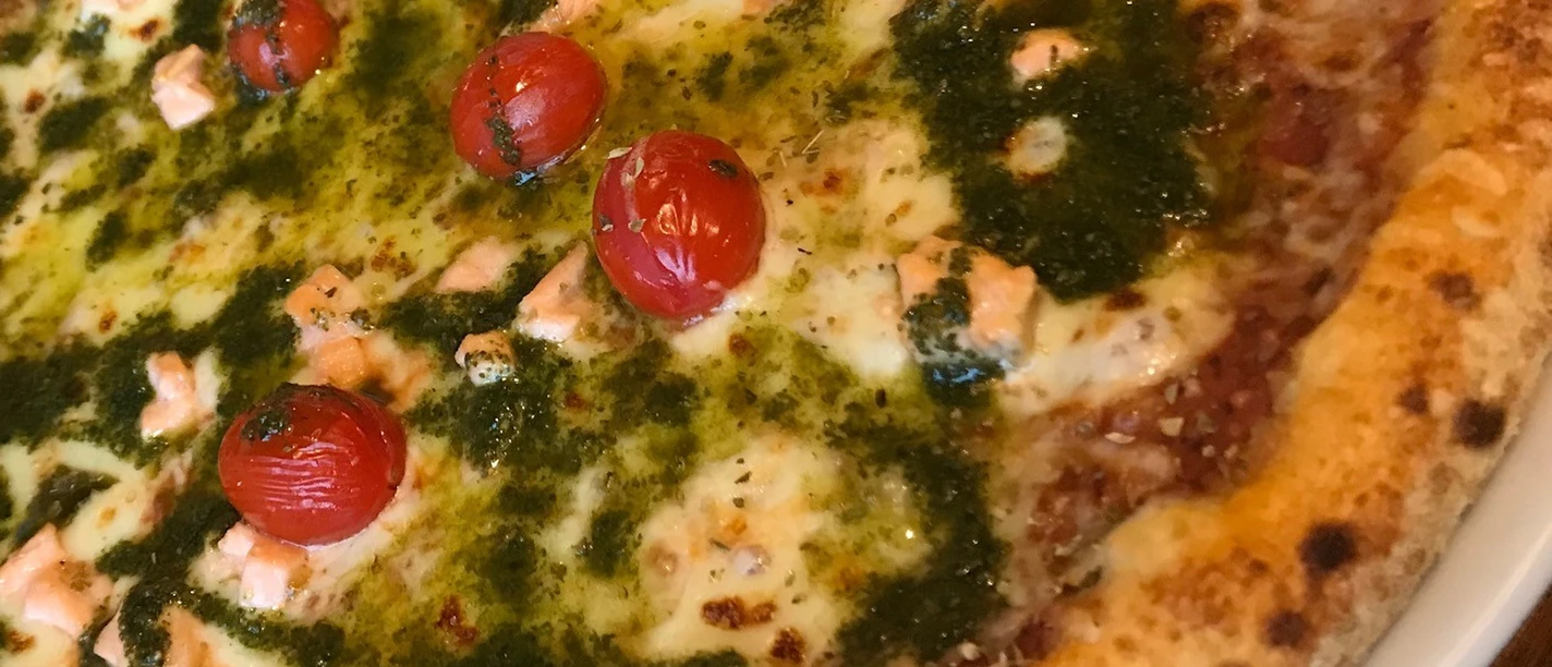 Pizza with melted cheese, fresh tomatoes, green pesto and salmon on a crispy base.