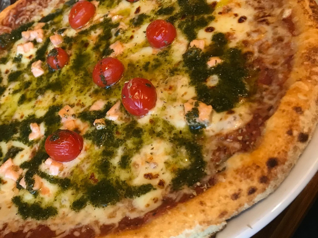 Pizza.jpg Pizza mit geschmolzenem Käse, frischen Tomaten, grüner Pesto und Lachs auf einem knusprigen Boden.