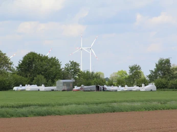 Segelflugverein Hoya Segelflugzeuge stehen auf einer grünen Wiese, im Hintergrund sind Bäume und ein Windrad zu sehen.