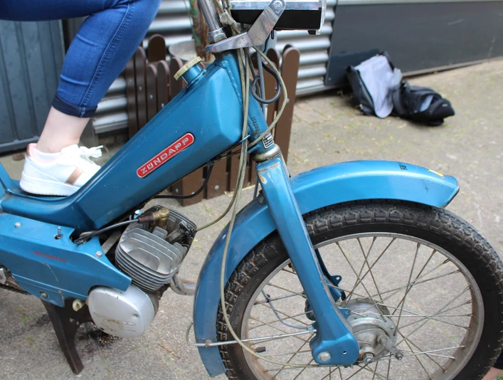 Mofa-Helden Ein blauer Zündapp-Mofa mit Reifenprofil, auf dem eine Person mit weißen Sneakern sitzt.