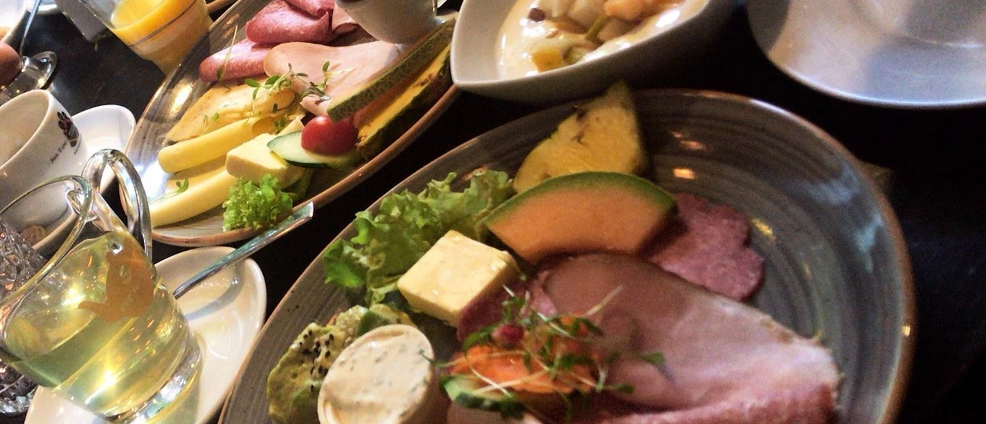 Various breakfast plates with cold cuts, cheese, fruit and bread rolls, coffee and juice.