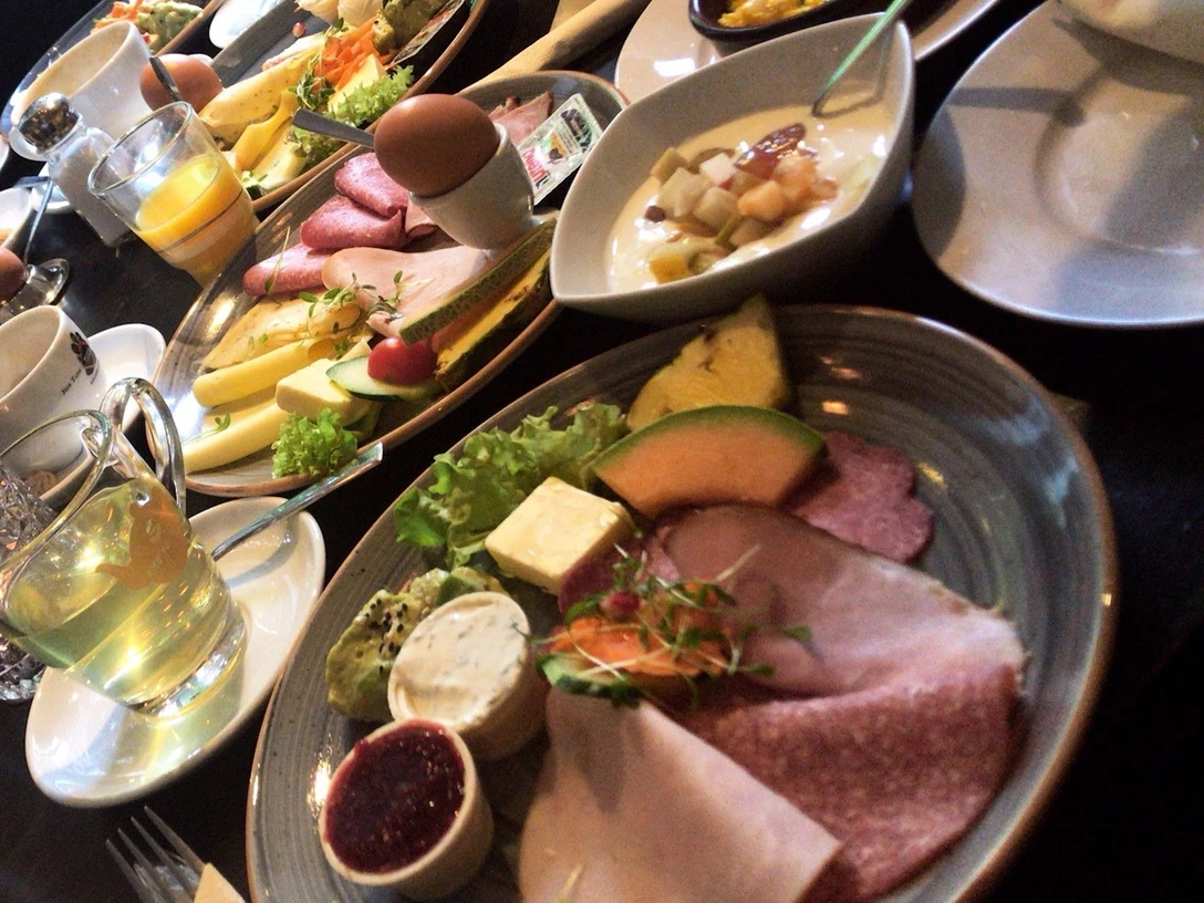 Frühstück Verschiedene Frühstücksteller mit Aufschnitt, Käse, Obst und Brötchen, daneben Kaffee und Saft.