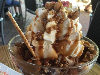 Ice cream sundae with cream, caramel, almonds, walnuts and a waffle on a wooden table.