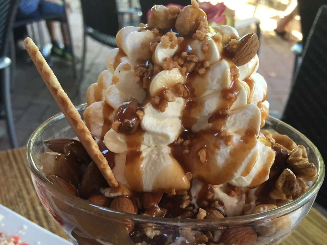 Eisbecher mit Sahne, Karamell, Mandeln, Walnüssen und einer Waffel auf einem Holztisch.Ice cream sundae with cream, caramel, almonds, walnuts and a waffle on a wooden table.Sundae med fløde, karamel, mandler, valnødder og en vaffel på et træbord.Sundae met room, karamel, amandelen, walnoten en een wafel op een houten tafel.
