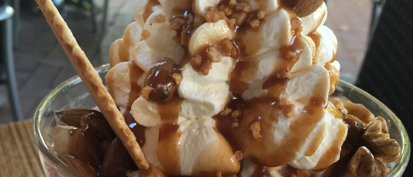 Ice cream sundae with cream, caramel, almonds, walnuts and a waffle on a wooden table.