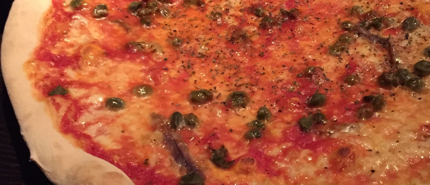A fresh pizza with a crispy crust, rich tomato sauce, capers and anchovy-speckled topping.