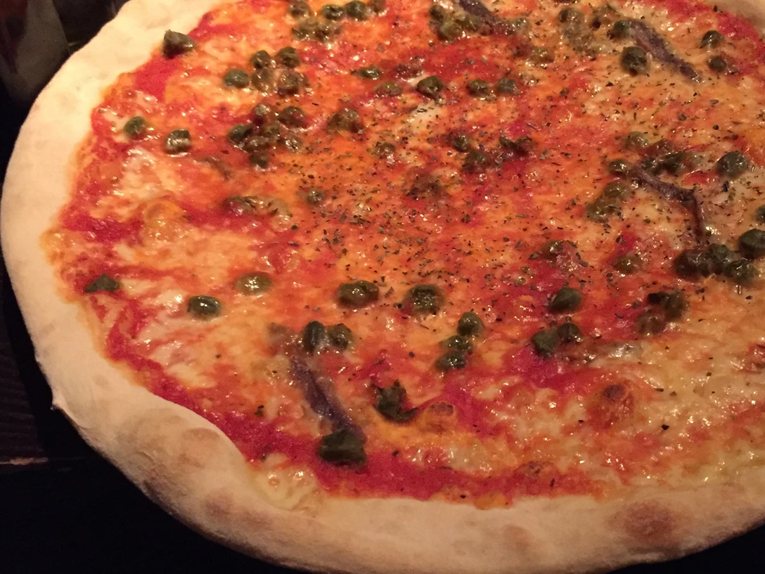 Pizza Eine frische Pizza mit knusprigem Rand, reichhaltigem Tomatensugo, Kapern und sardellengesprenkeltem Belag.