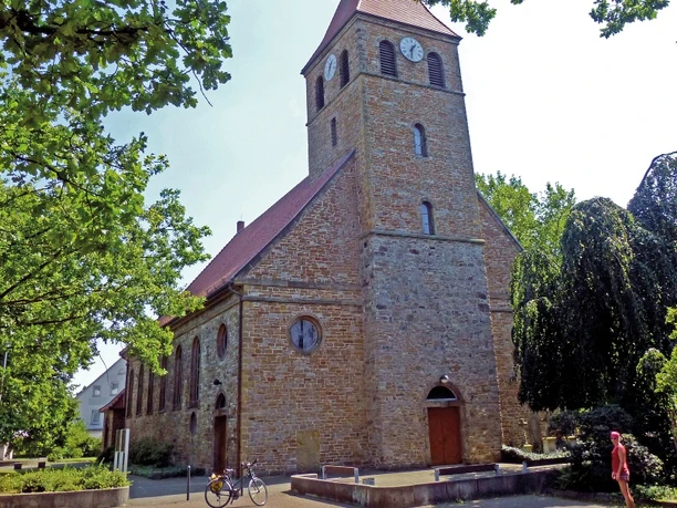 Kirche Kirchlengern Eine alte, aus Stein gebaute Kirche mit Turm, umgeben von Bäumen, mit zwei Fahrrädern davor.
