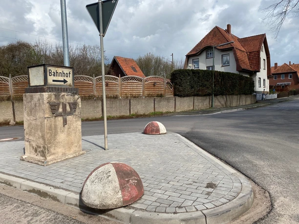 Bahnhof Leese-Stolzenau Straßenkreuzung mit Wegweiser zum Bahnhof Leese-Stolzenau, umgeben von Wohnhäusern und Natur.