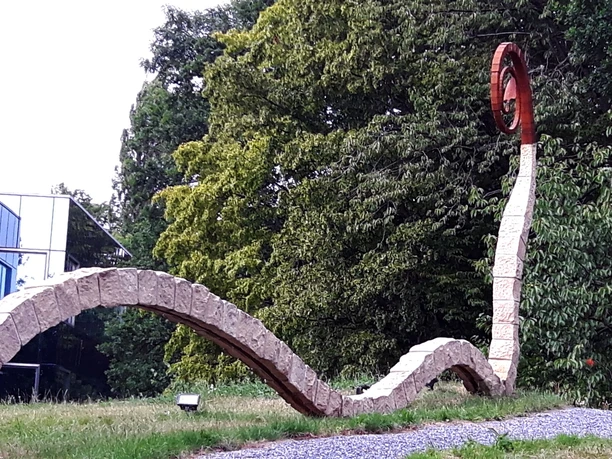 Skulpturenpark Moderne Skulptur in einem Park, geschwungene Formen aus Stein und Metall, umgeben von Bäumen.