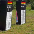Drei große schwarze Säulen mit weißen Texttafeln über Artikel des Grundgesetzes in einem grünen Park.