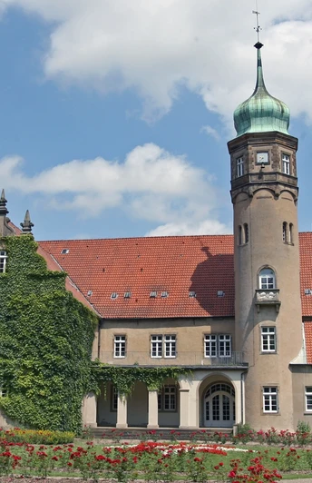 Ein historisches Wasserschloss mit markantem Rundturm, roten Dächern und von Efeu bewachsen.