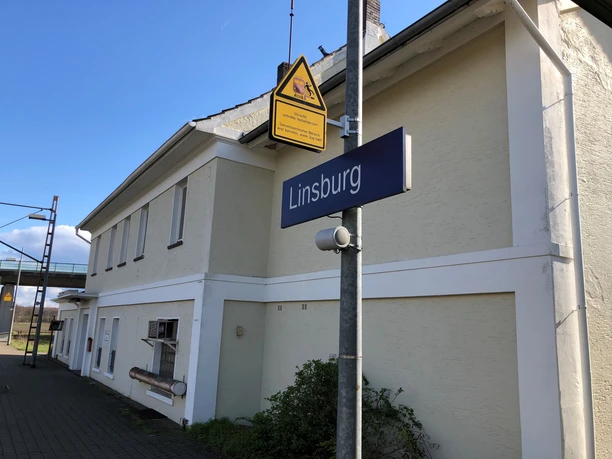 Ein zweistöckiges Bahnhofsgebäude in Linsburg mit gelblichem Anstrich und einem blauen Schild.
