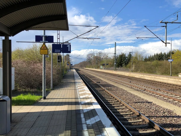 Bahnhof Linsburg: Moderner Bahnsteig mit Gleisen und Wartebereich, umgeben von grünen Büschen.