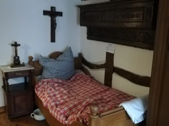 Schlafzimmer der Magd Ein einfaches Schlafzimmer mit Einzelbett, kariertem Bettzeug und hölzernen Möbeln auf Holzboden.
