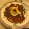 Schnitzel Teller Goldbraun paniertes Schnitzel, garniert mit Petersilie und zwei Zitronenscheiben auf floralem Teller.