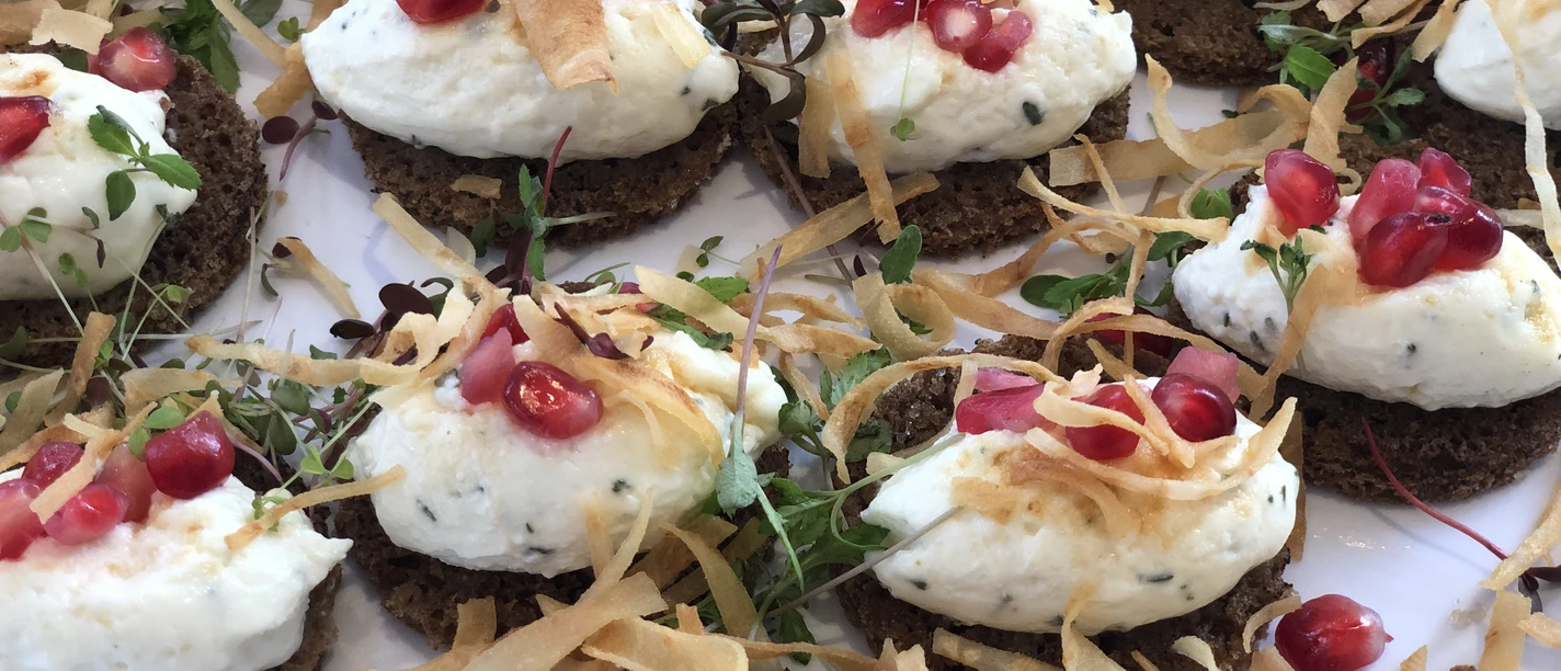 Kalte Platte Eine Ansammlung von Roggenbrotscheiben, belegt mit cremigem Käse und garniert mit Granatapfelkernen.