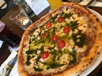 Pizza on a plate, garnished with juicy cheese, fresh cherry tomatoes and green basil pesto.