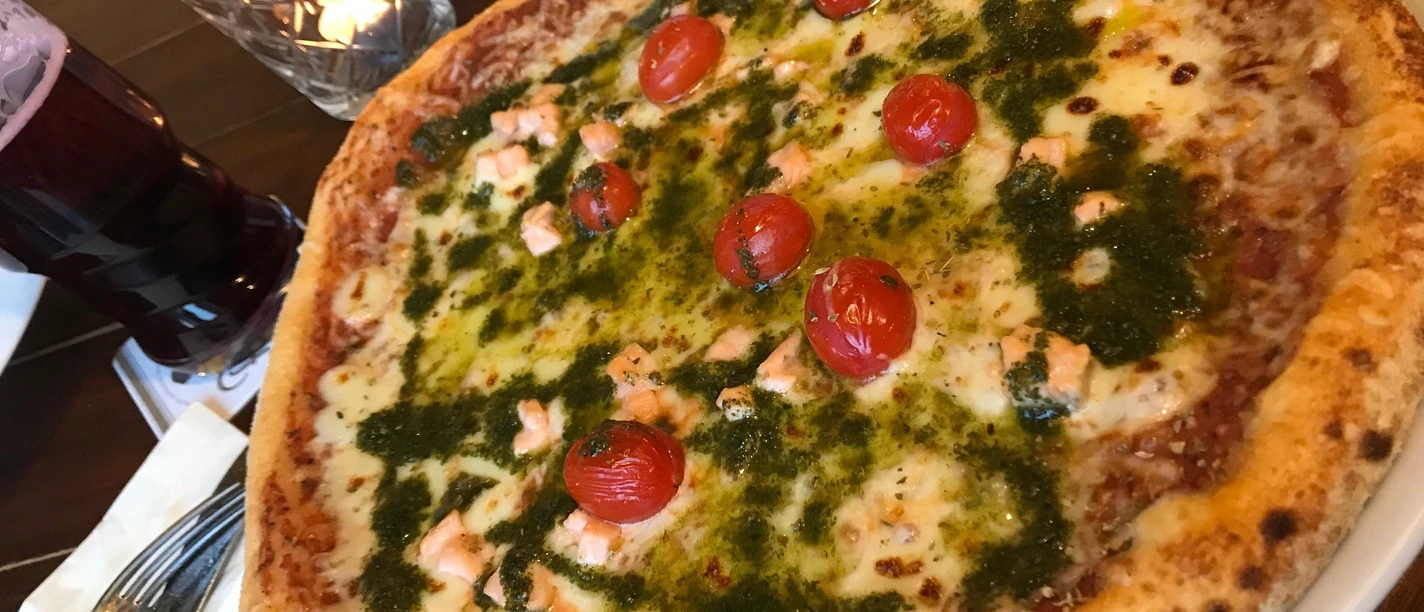 Pizza on a plate, garnished with juicy cheese, fresh cherry tomatoes and green basil pesto.