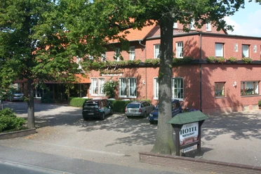 Rodes Hotel Rotes Backsteingebäude mit Hotelbeschriftung, umgeben von Bäumen und geparkten Autos im Vordergrund.