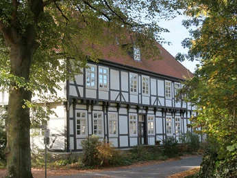 Herrenhaus Stift Quernheim Historisches Fachwerkhaus umgeben von Bäumen, mit rotem Dach und weißen Fensterrahmen im Sonnenschein.