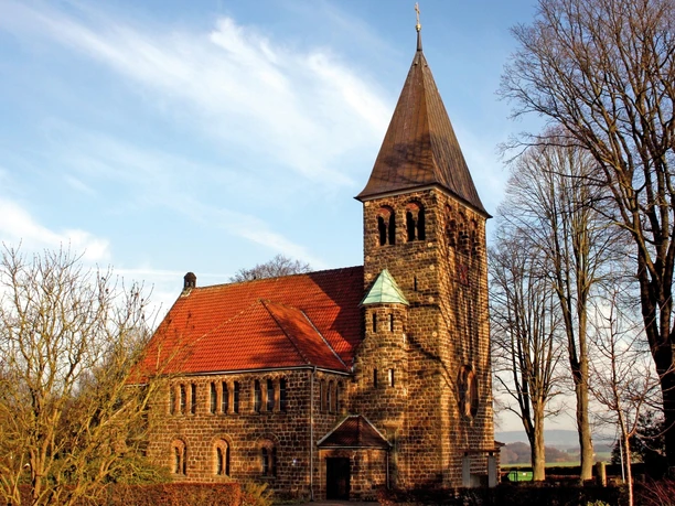 Backsteinkirche Hagedorn mit markantem Turm umgeben von kahlen Bäumen an einem sonnigen Tag.