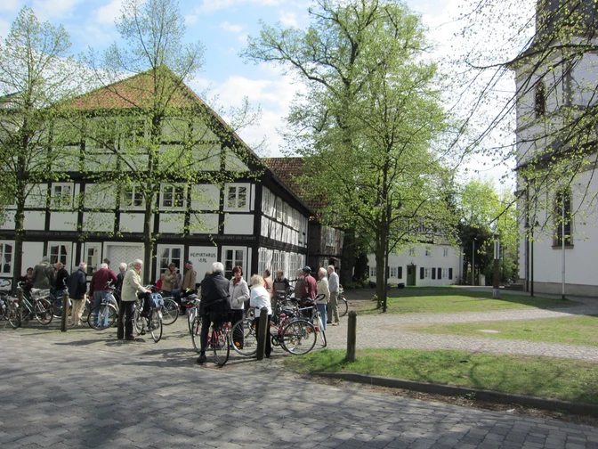 Radfahrende vor dem Heimathaus am Kirchplatz Eine Gruppe von Menschen mit Fahrrädern steht vor historischen Fachwerkhäusern in grüner Umgebung.