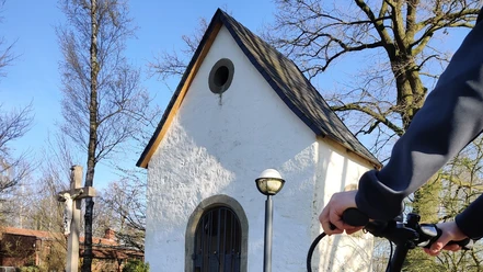Fahrradfahrer vor der Seppeler-Kapelle Eine Person auf einem Fahrrad vor einer kleinen, weißen Kapelle mit spitzem Dach und Holzkreuz.