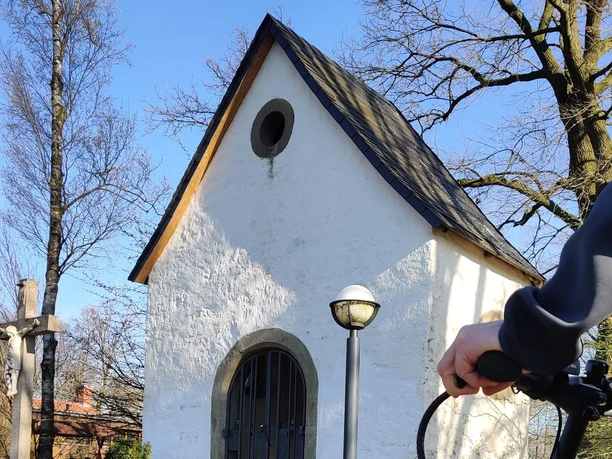 Fahrradfahrer vor der Seppeler-Kapelle Eine Person auf einem Fahrrad vor einer kleinen, weißen Kapelle mit spitzem Dach und Holzkreuz.