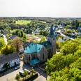 Sankt Georg Seelscheid Die Kirche in Neunkirchen-Seelscheid steht majestätisch von Bäumen umgeben, mit Häusern im Hintergrund.