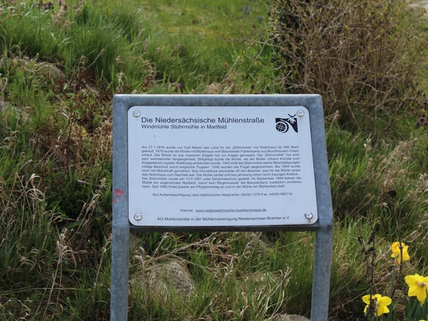 Gedenktafel der Windmühle Stührmühle in Martfeld auf einer grünen Wiese, umgeben von Natur.