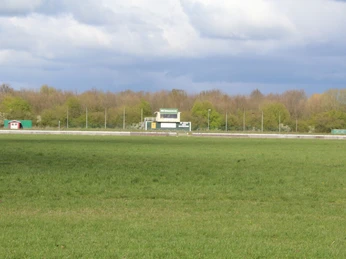 Rennbahn Schwarme Weite, grüne Rasenfläche vor einer Pferderennbahn, umgeben von Bäumen, mit einem Scoreboard.