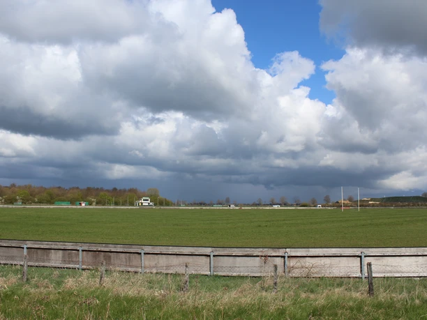 Weite grüne Wiese der Rennbahn Schwarme unter einem teilweise bewölkten blauen Himmel.