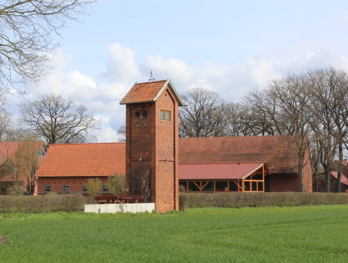 Trafohäuschen Anderten Ein altes, rotes Backstein-Trafohäuschen steht inmitten einer grünen Landschaft vor bäuerlichen Gebäuden.