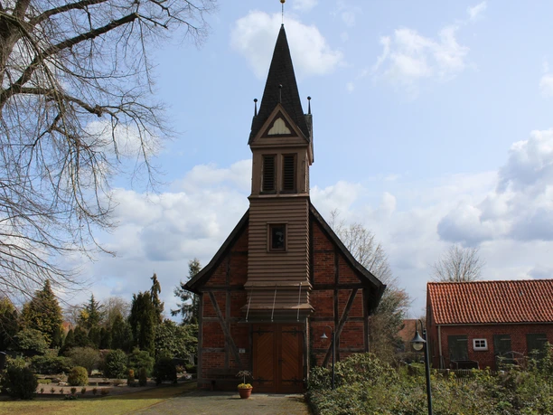 A historic half-timbered chapel with a striking tower, surrounded by well-maintained gardens.