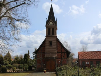 Fachwerkkapelle Anderten Eine historische Fachwerkkapelle mit markantem Turm, umgeben von einer gepflegten Gartenanlage.