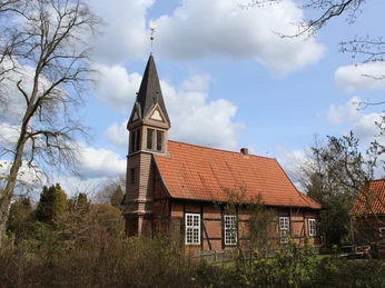 Fachwerkkapelle Anderten Fachwerkkapelle Anderten umgeben von blühenden Bäumen, mit markantem Turm und blauer Himmel im Hintergrund.