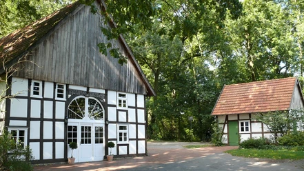Bunten Mühle Fachwerkhaus mit großem Eingang und kleineres Nebengebäude, umgeben von üppigem Grün.
