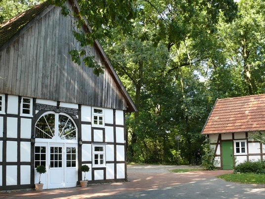 Bunten Mühle Fachwerkhaus mit großem Eingang und kleineres Nebengebäude, umgeben von üppigem Grün.