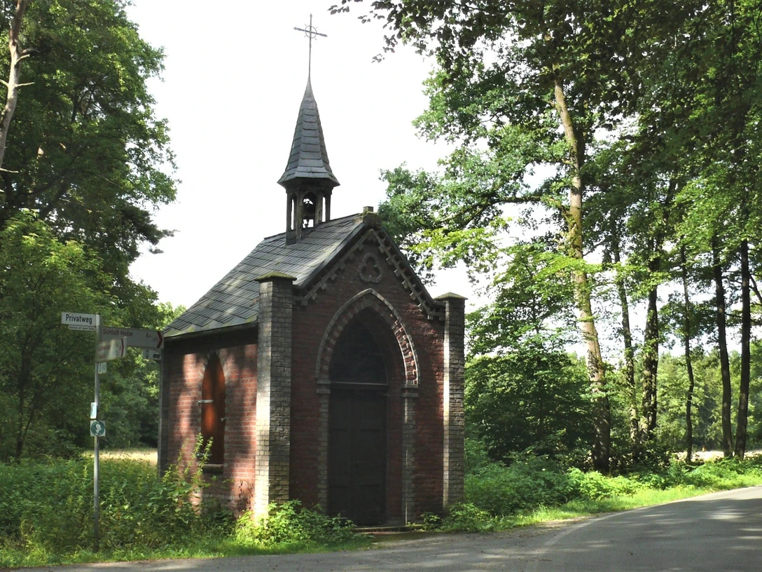 Markuskapelle Eine kleine, historische Kapelle aus Backstein mit spitzem Turm steht umgeben von grünem Wald.