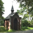 Markuskapelle Eine kleine, historische Kapelle aus Backstein mit spitzem Turm steht umgeben von grünem Wald.