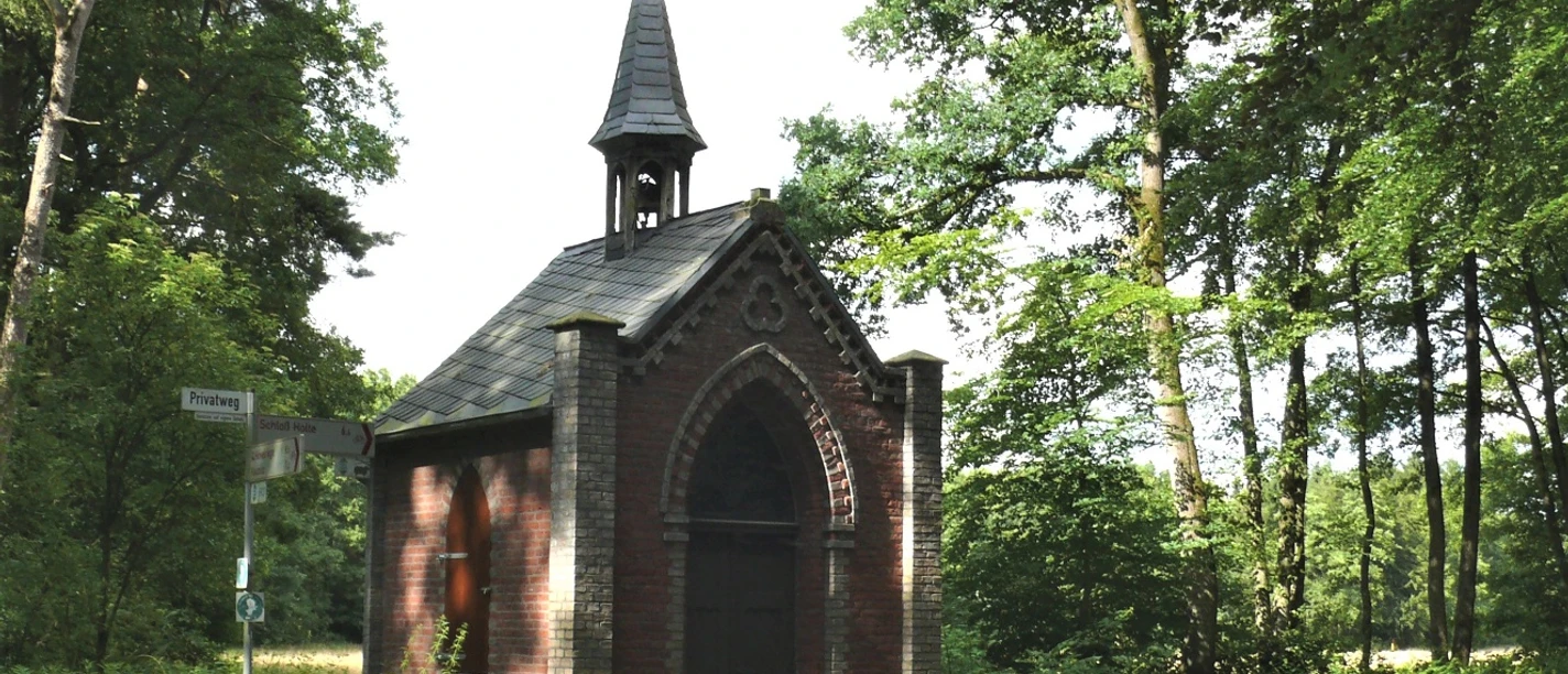 Markuskapelle Eine kleine, historische Kapelle aus Backstein mit spitzem Turm steht umgeben von grünem Wald.