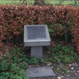 Gedenktafel Steinplatte mit Gravur, umgeben von herbstlich verfärbten Buchenhecken, steht auf grasbewachsenem Boden.