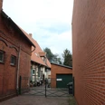 Backsteingebäude mit rotem Dach und Tor zu Hof, links ein Baum, rechts ein moderner Anbau.Brick building with red roof and gate to the courtyard, a tree on the left, a modern extension on the right.Murstensbygning med rødt tag og port til gårdspladsen, et træ til venstre, en moderne tilbygning til højre.Bakstenen gebouw met rood dak en poort naar de binnenplaats, een boom aan de linkerkant, een moderne aanbouw aan de rechterkant.